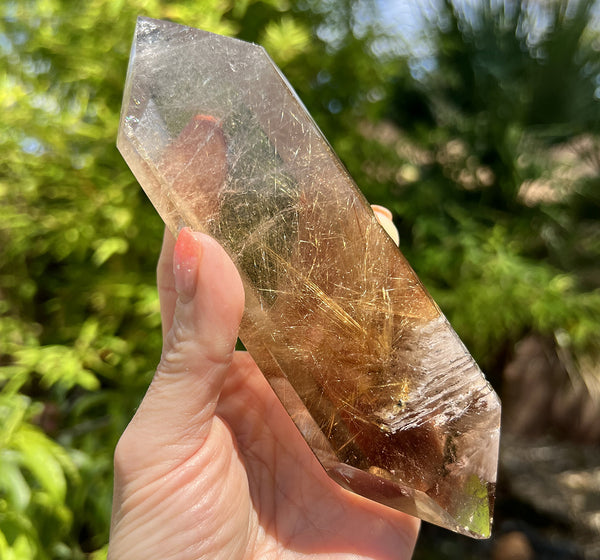 Image of a hand holding a rare rutilated smoky quartz crystal that's double terminated.