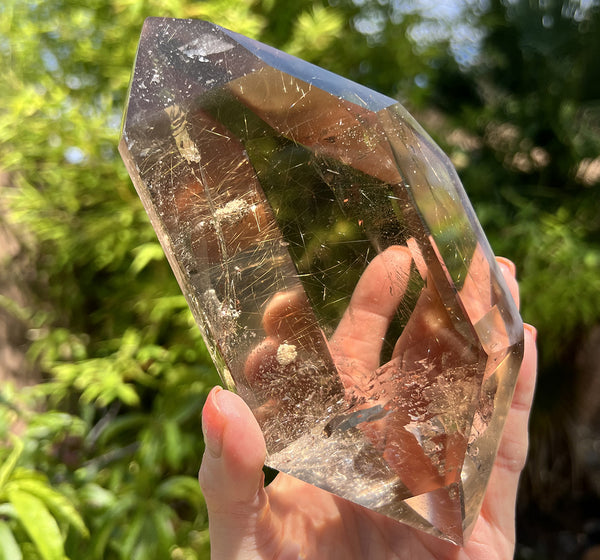 Image of a hand holding a rare rutilated smoky quartz crystal that's double terminated.