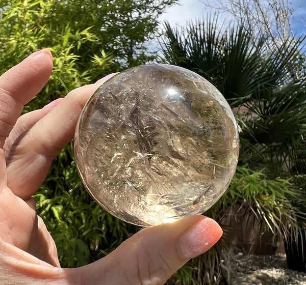 Image of a hand holding a smoky quartz crystal sphere. 
