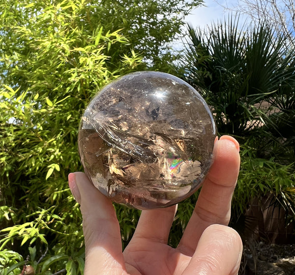 Image of a hand holding a smoky quartz crystal sphere. 