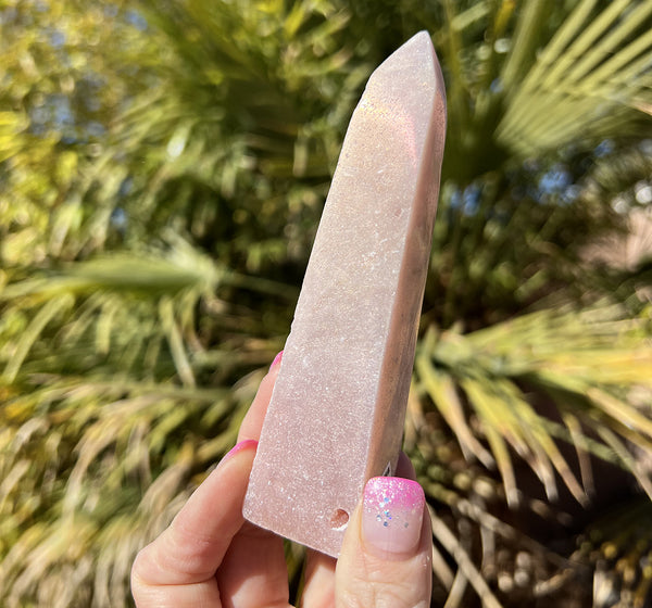 Image of a hand holding a aura pink amethyst obelisk crystal.