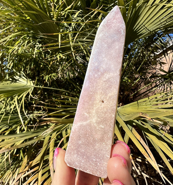 Image of a hand holding a aura pink amethyst obelisk crystal.