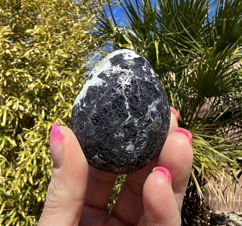 Image of a hand holding a covellite crystal egg.  