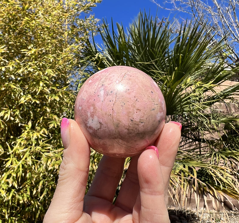 Image of a hand holding a rhodonite sphere.