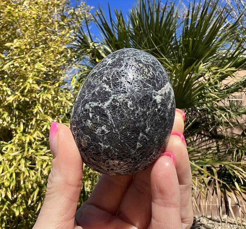 Image of a hand holding a covellite crystal egg.  