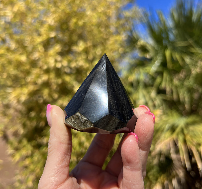 Image of a hand holding a golden sheen obsidian chakra extractor.