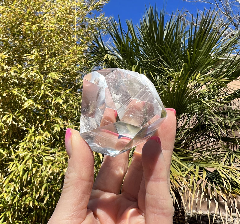 Image of a hand holding a Diamantine faceted quartz crystal. 