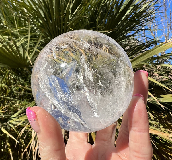 Image of a hand holding a clear quartz sphere. 